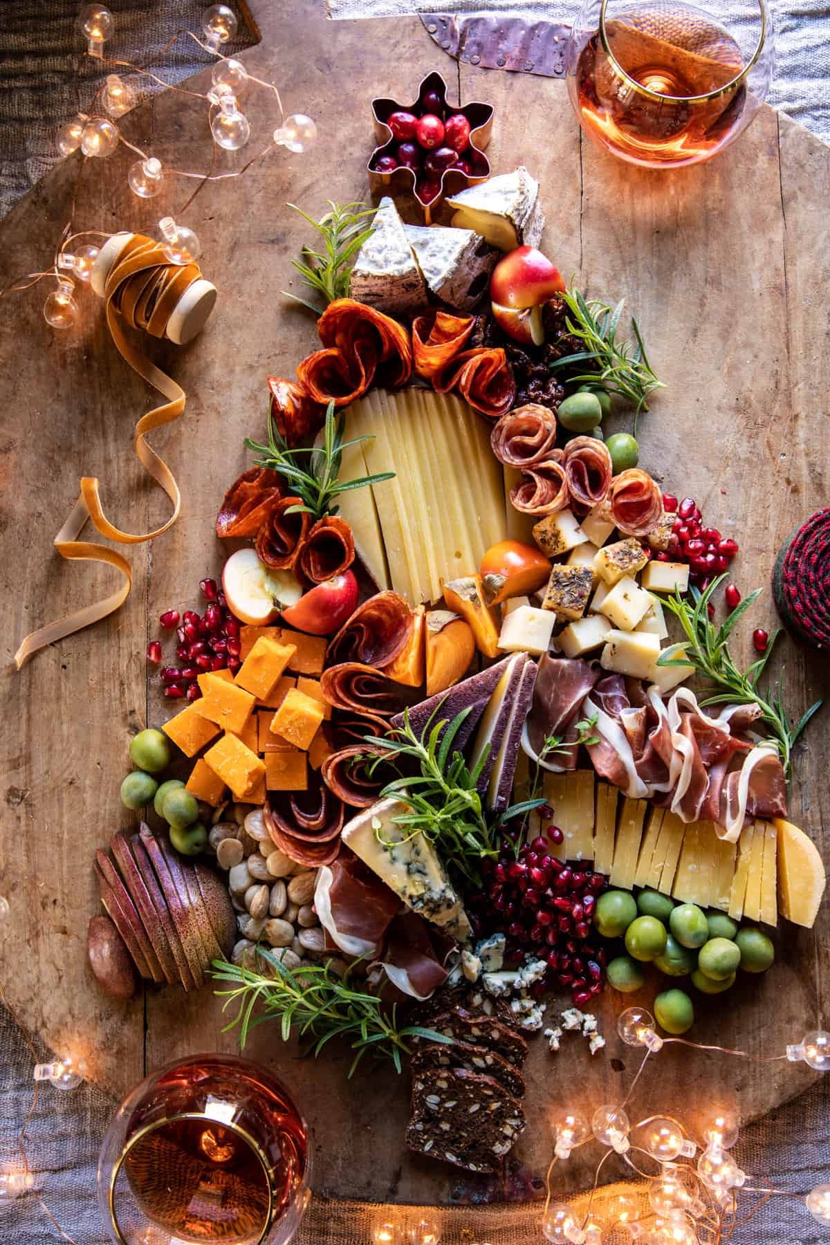 A Christmas tree board of cheeses, prosciutto and rosemary on a rustic table.
