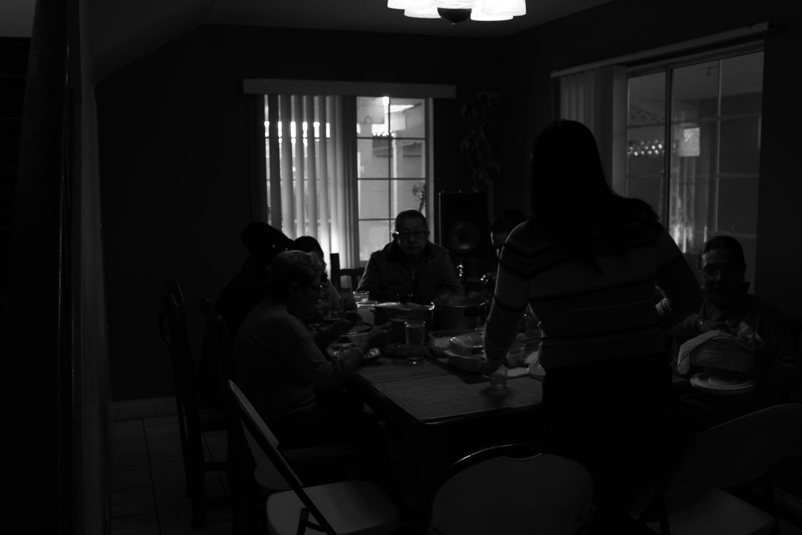 A small group of friends around a rustic dining table in a warmly lit home kitchen.