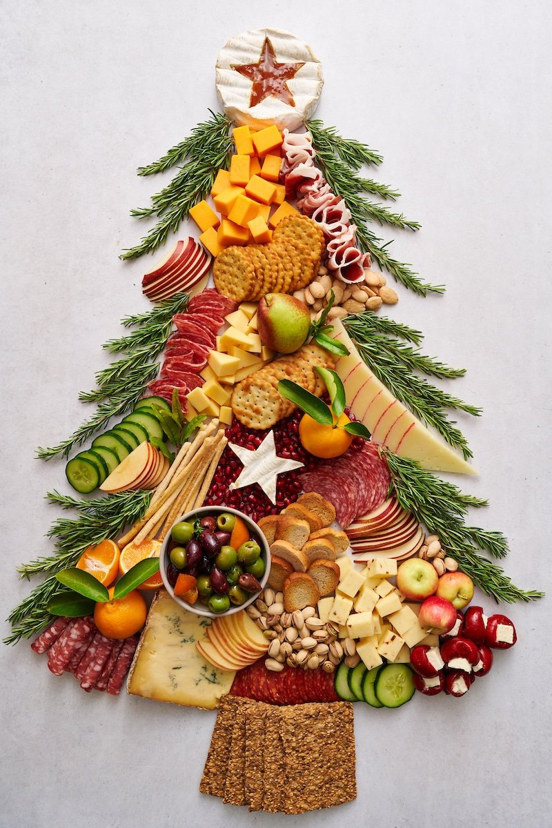 A Christmas tree board with crackers, cheeses, cured meats and vegetables.