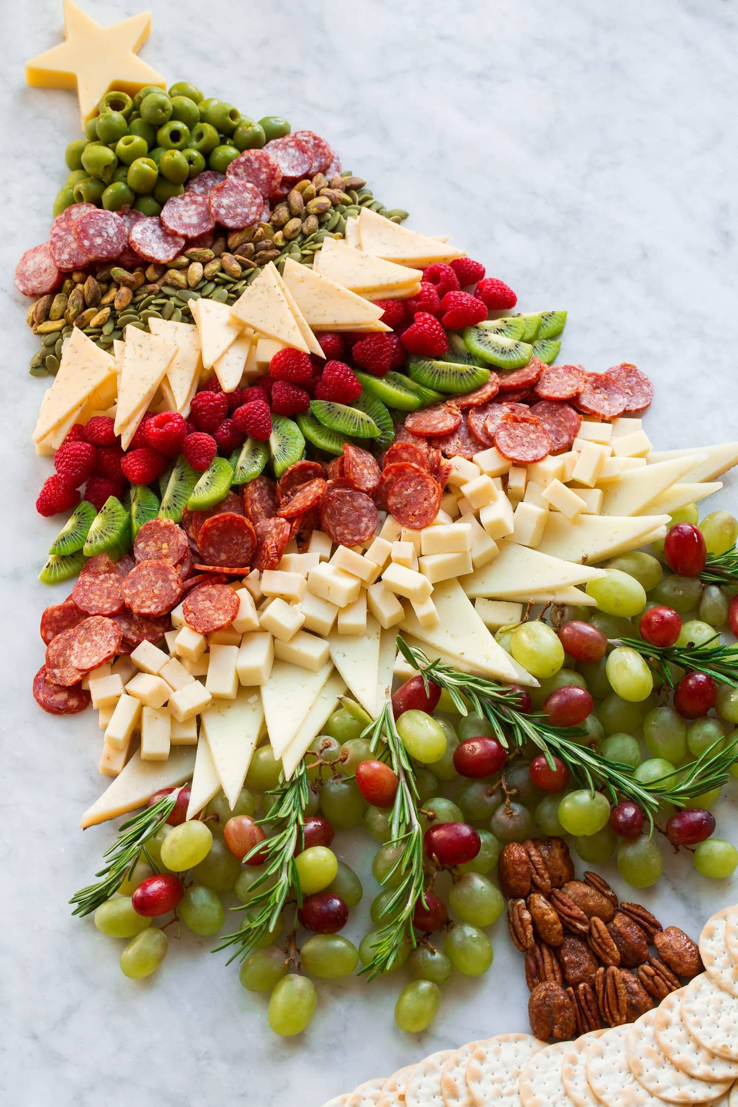 A charcuterie board shaped like a Christmas tree, layered with cheeses, salami, grapes and rosemary.